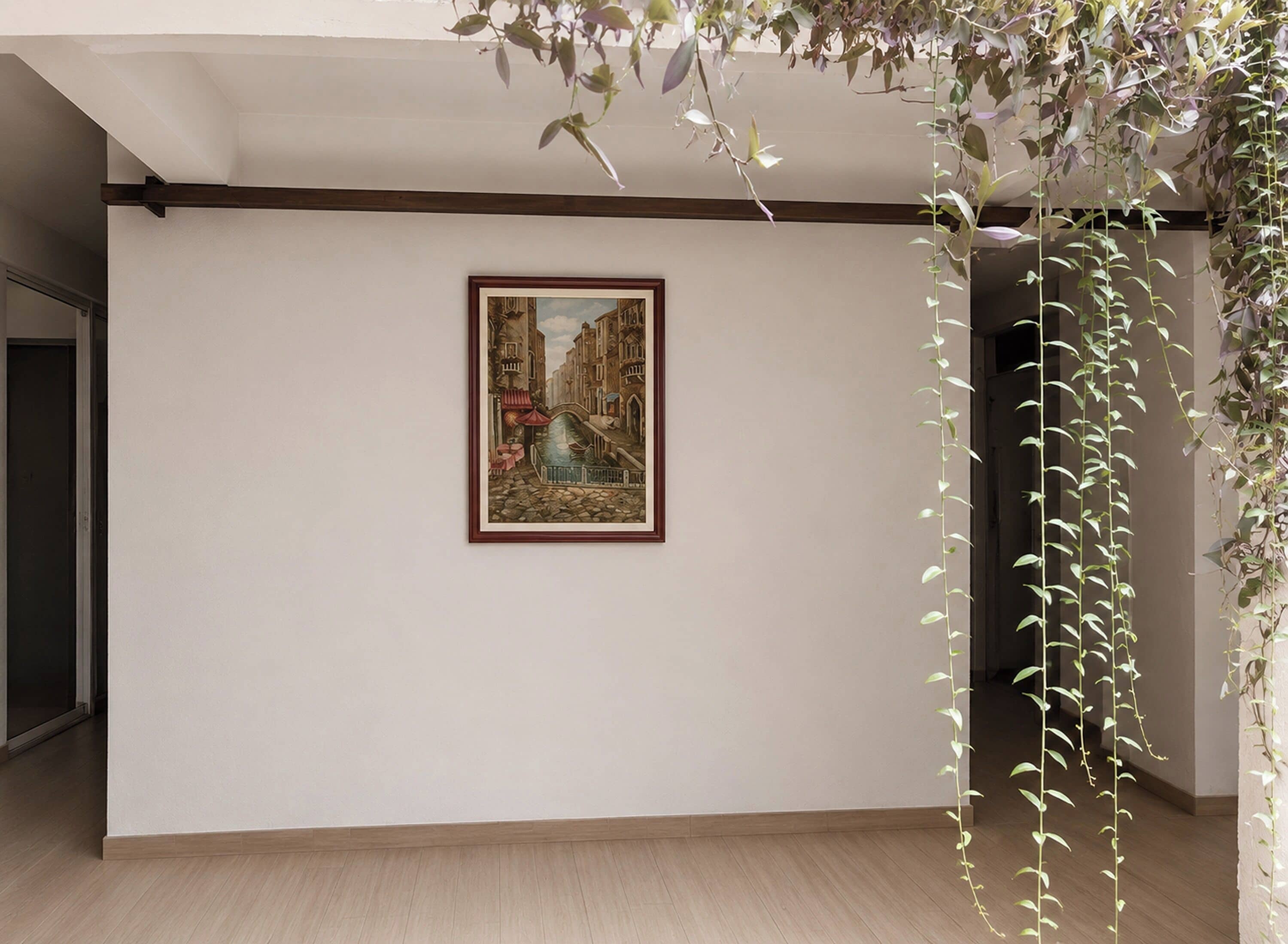 Una habitación con un cuadro enmarcado, piso de madera y plantas colgantes.