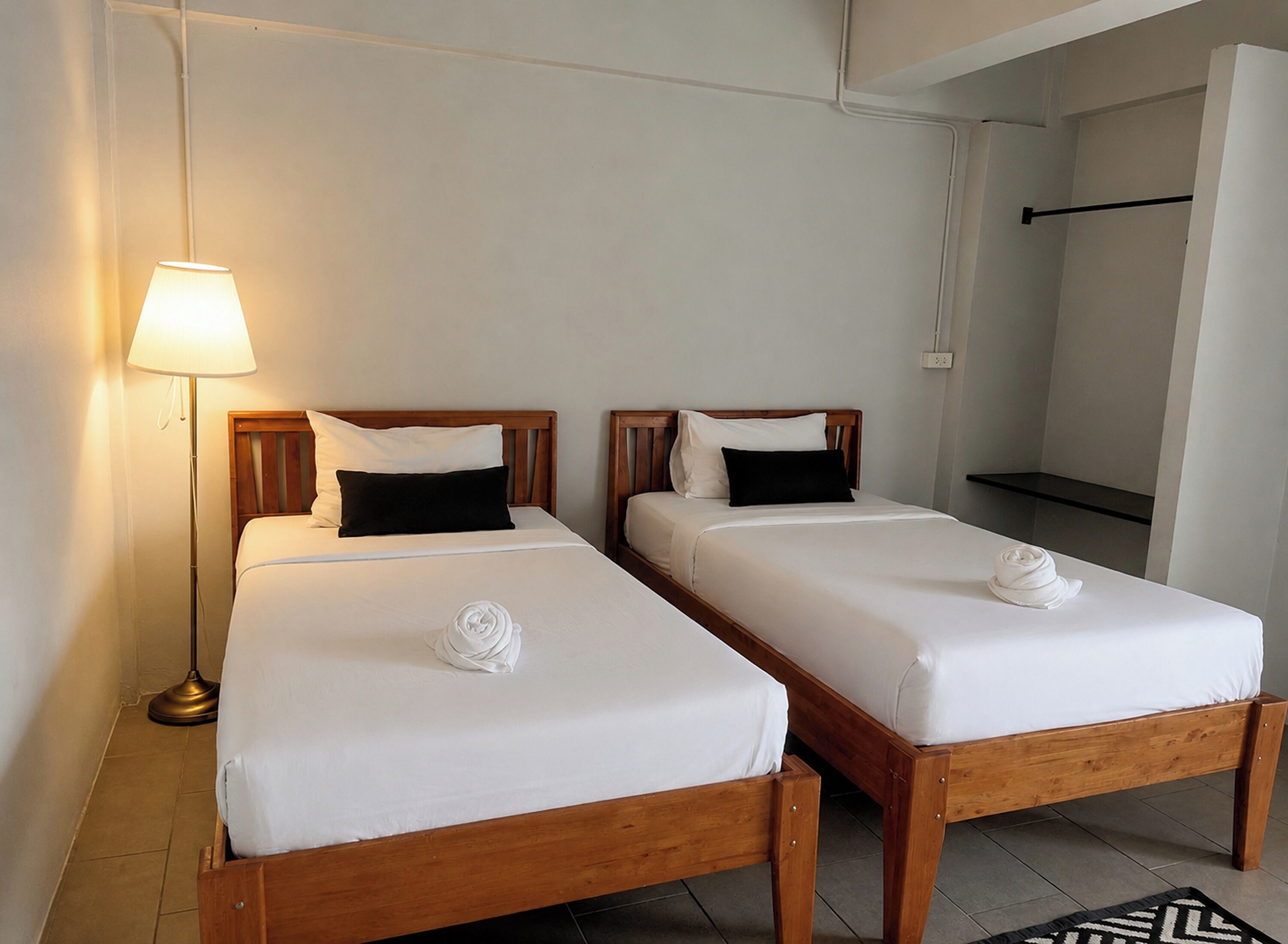 Two single beds with wooden frames, white bedding, black pillows, a floor lamp, and a black and white rug.