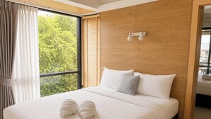 A modern hotel room with a large bed, a wooden headboard, and a view of greenery through the window. - Palmari Boutique Hotel (Nuea Khlong)