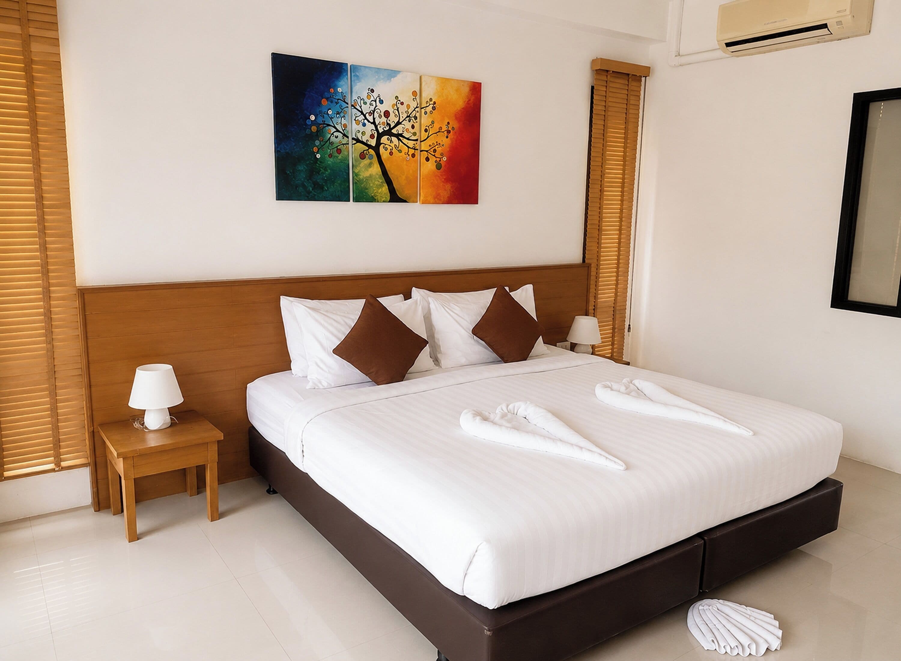 Une chambre d’hôtel avec un grand lit, une table de chevet avec une lampe, un tableau au mur et une fenêtre avec des stores.