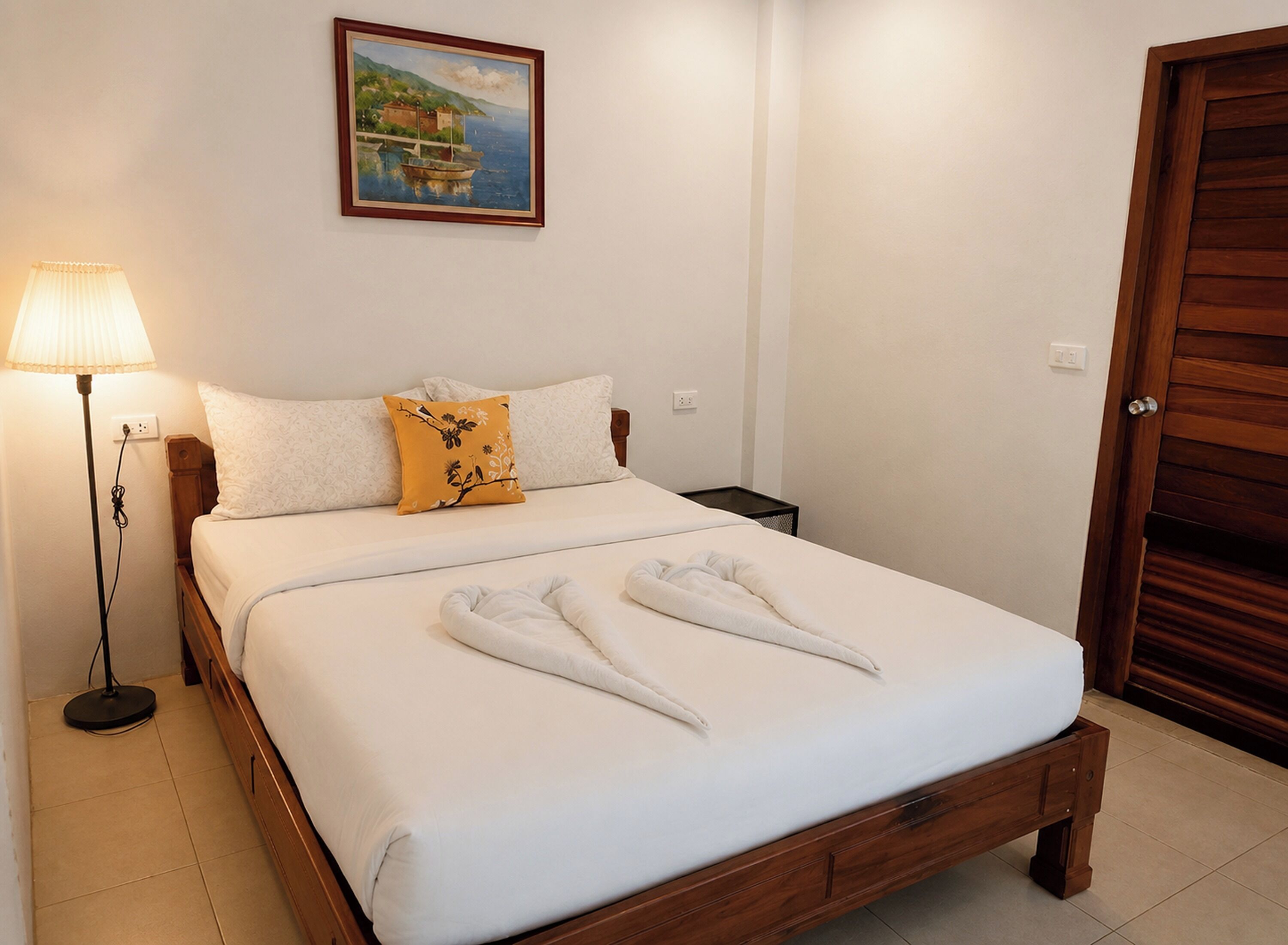 A neatly made bed with white linens, a single yellow pillow, and two white towels folded on the bed.