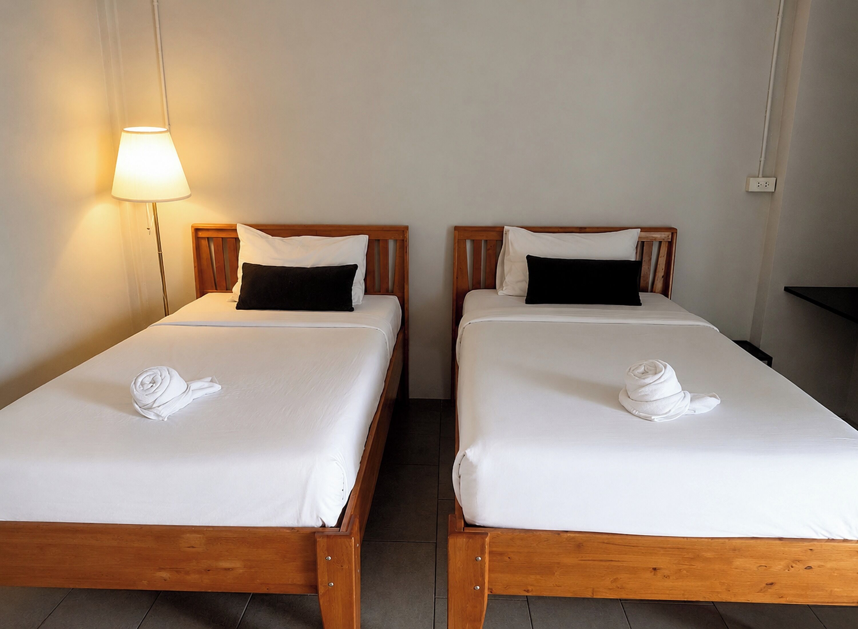 Dos camas individuales con cabeceros de madera, ropa de cama blanca y almohadas negras.