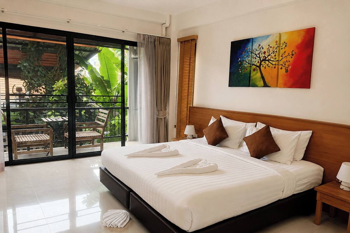 Een hotelkamer met een groot bed, uitzicht op groen door een schuifdeur en een schilderij aan de muur.