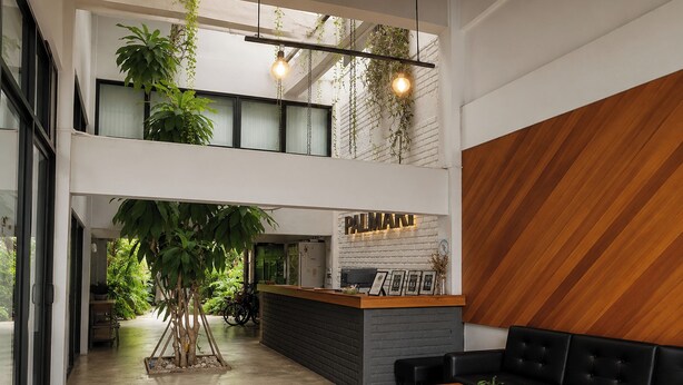 A modern hotel lobby with a reception desk, seating area, and a large indoor plant. - Palmari Boutique Hotel (Nuea Khlong)