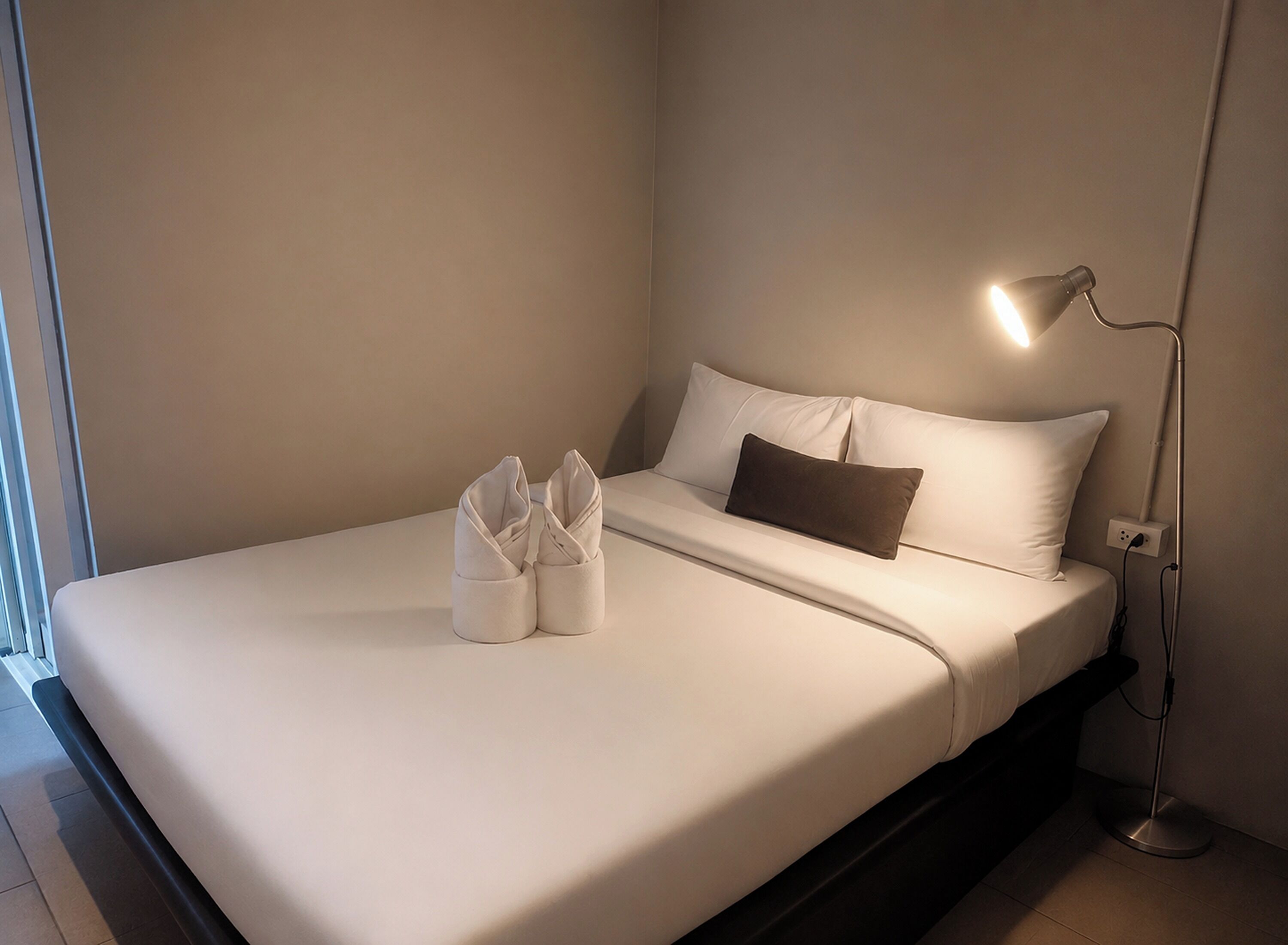 A neatly made bed with pillows, a bedside lamp, and a pair of folded towels on the bed.