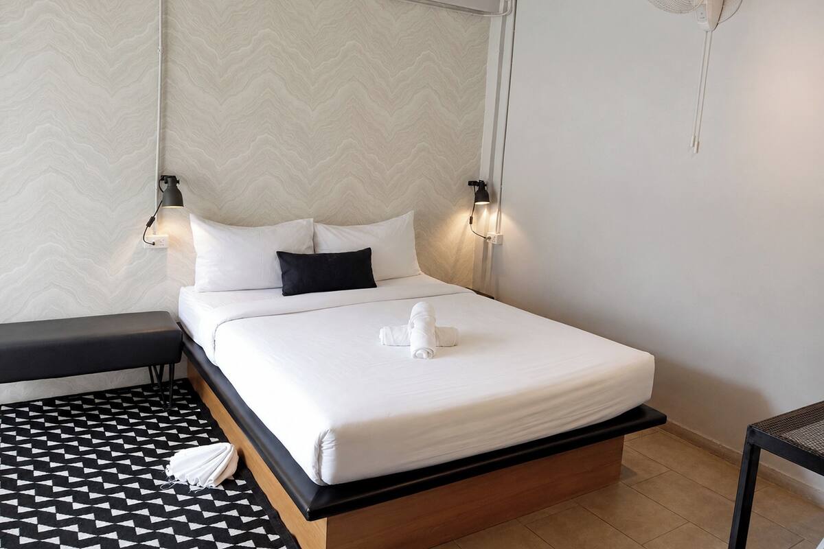 Een hotelkamer met een bed, nachtlampjes, een ventilator aan de muur en een kamer met een patroon op de vloer.