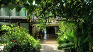 A pathway flanked by lush greenery and potted plants, leading to a building entrance. - Palmari Boutique Hotel (Nuea Khlong)