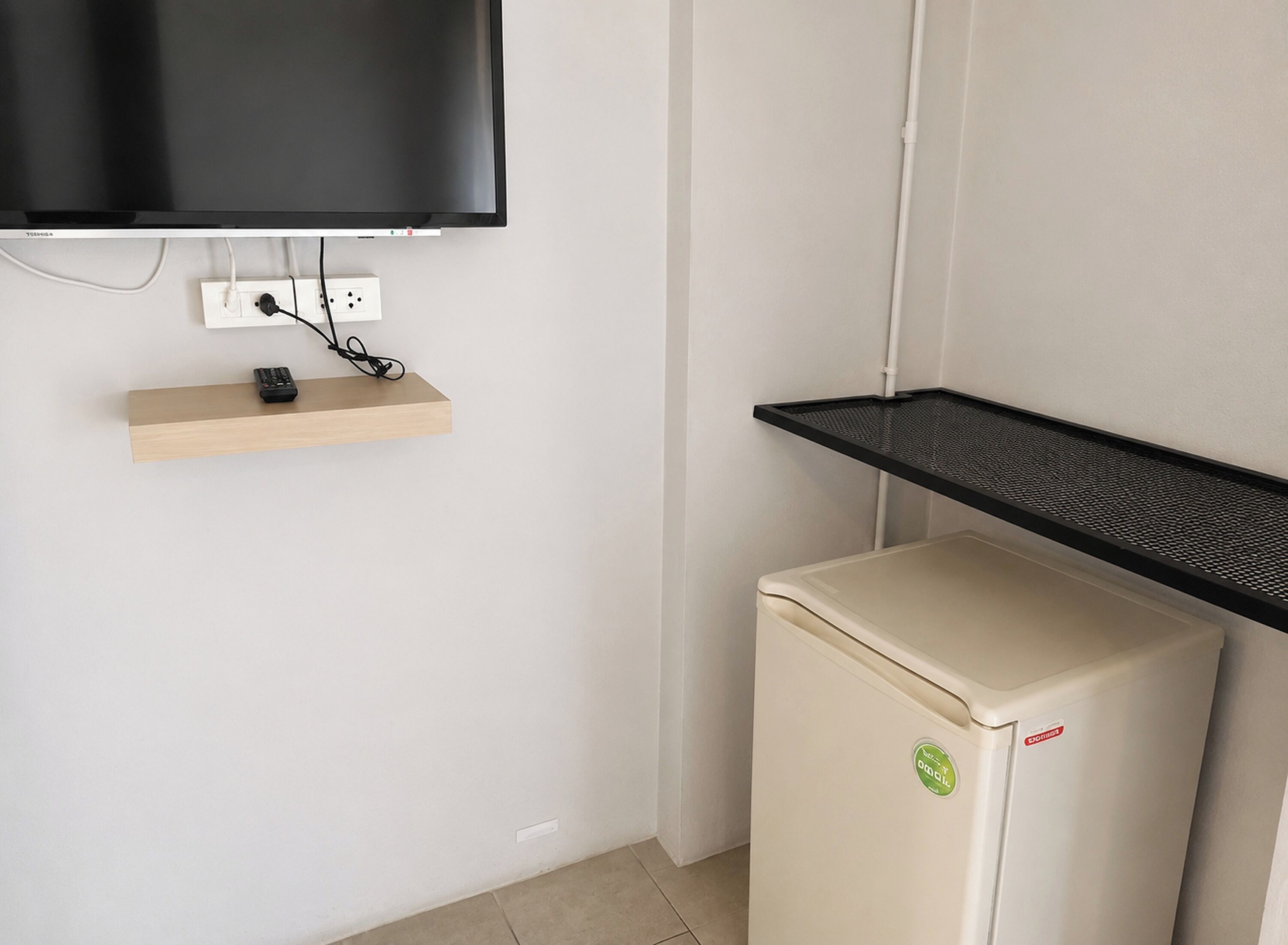 Ein kleiner Raum mit einem an der Wand montierten Fernseher, einer Steckdose, einem Holzregal und einem Kühlschrank.