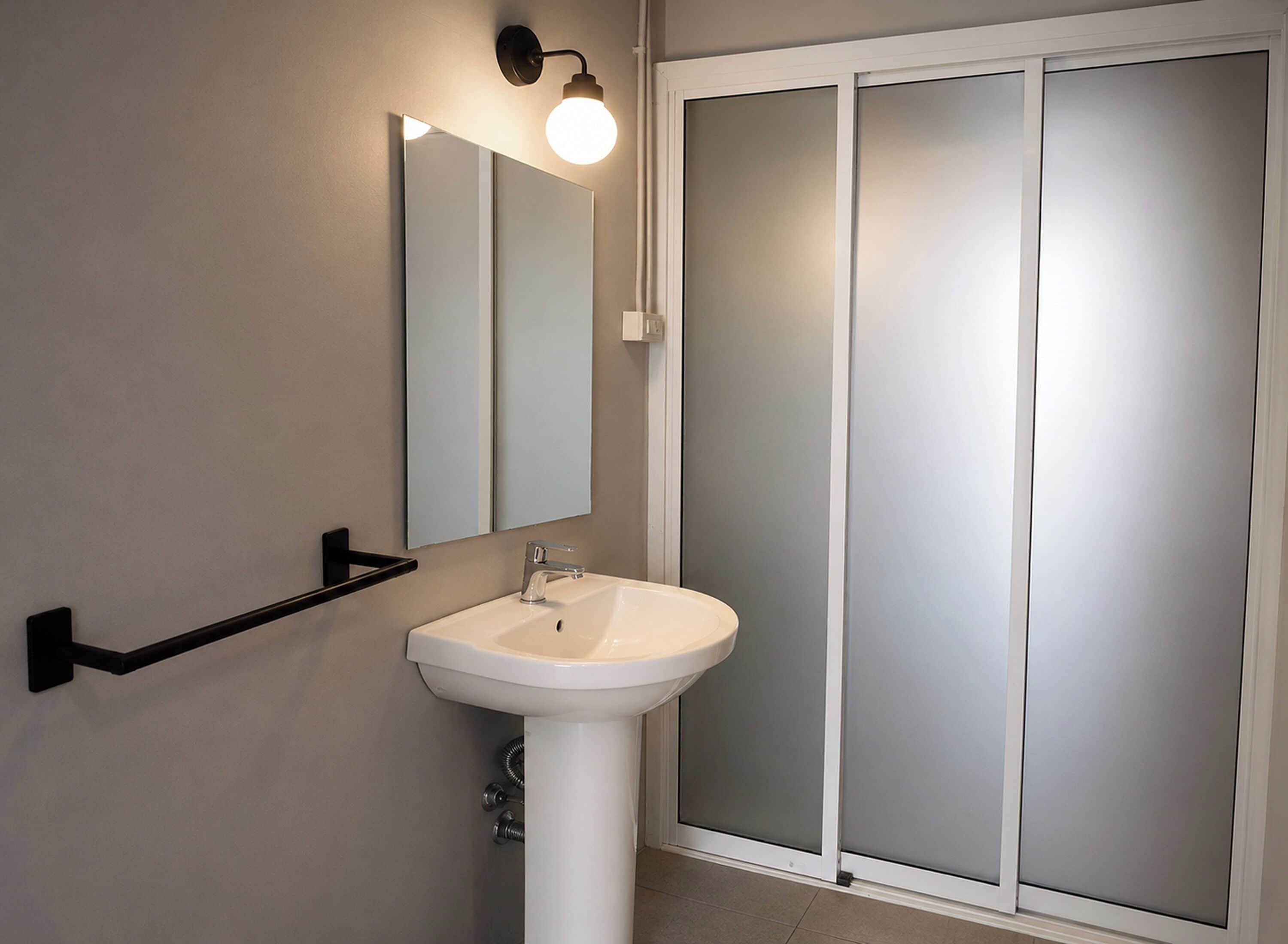 Un baño con un lavamanos blanco, un espejo y una puerta de vidrio esmerilado.