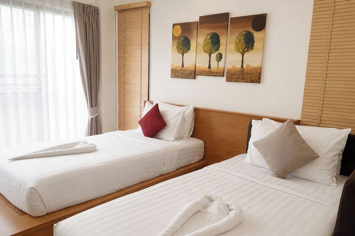 Een hotelkamer met twee bedden, een houten hoofdeinde, een raam met gordijnen, en drie schilderijen aan de muur.
