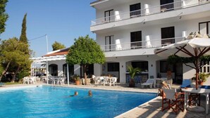 Ein Swimmingpool mit Liegestühlen und Sonnenschirmen, umgeben von einem Gebäude mit Balkonen und Außenbereich.