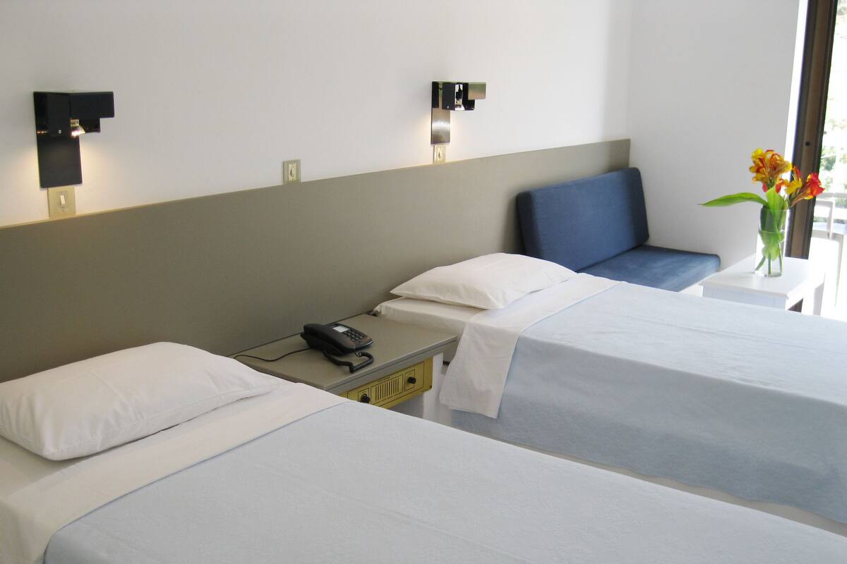 Hotellihuone, jossa on kaksi sänkyä, yöpöytä, jossa on puhelin, tuoli ja maljakko, jossa on kukkia.