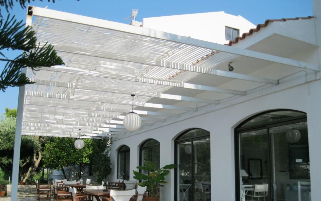 A covered outdoor seating area with tables and chairs, large windows, and a white building facade.