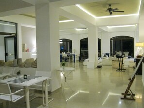 A modern living room with a white color scheme, a dining area with a white table and chairs, and a ceiling fan. - Hotel Apollon (Samos)