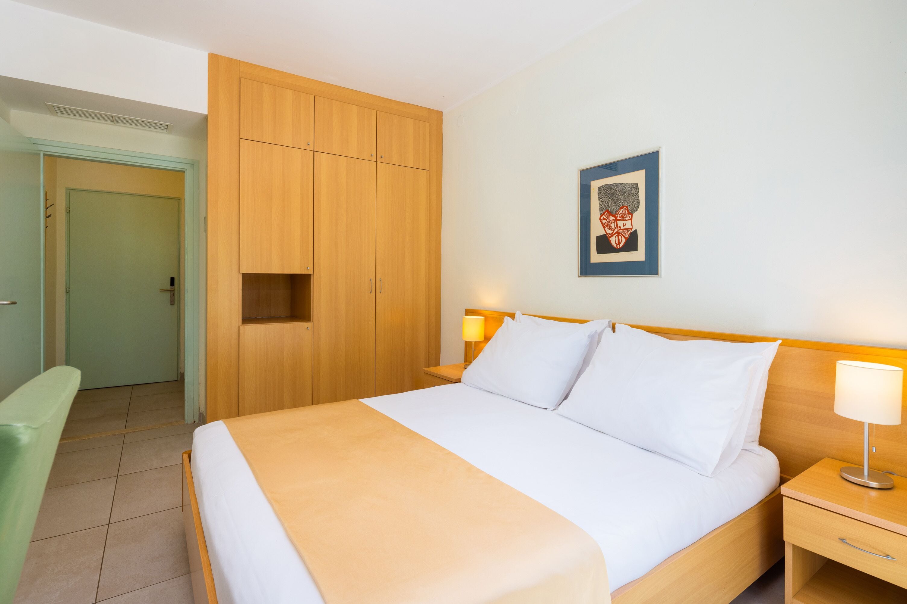 A hotel room with a bed, bedside table, and a wardrobe.