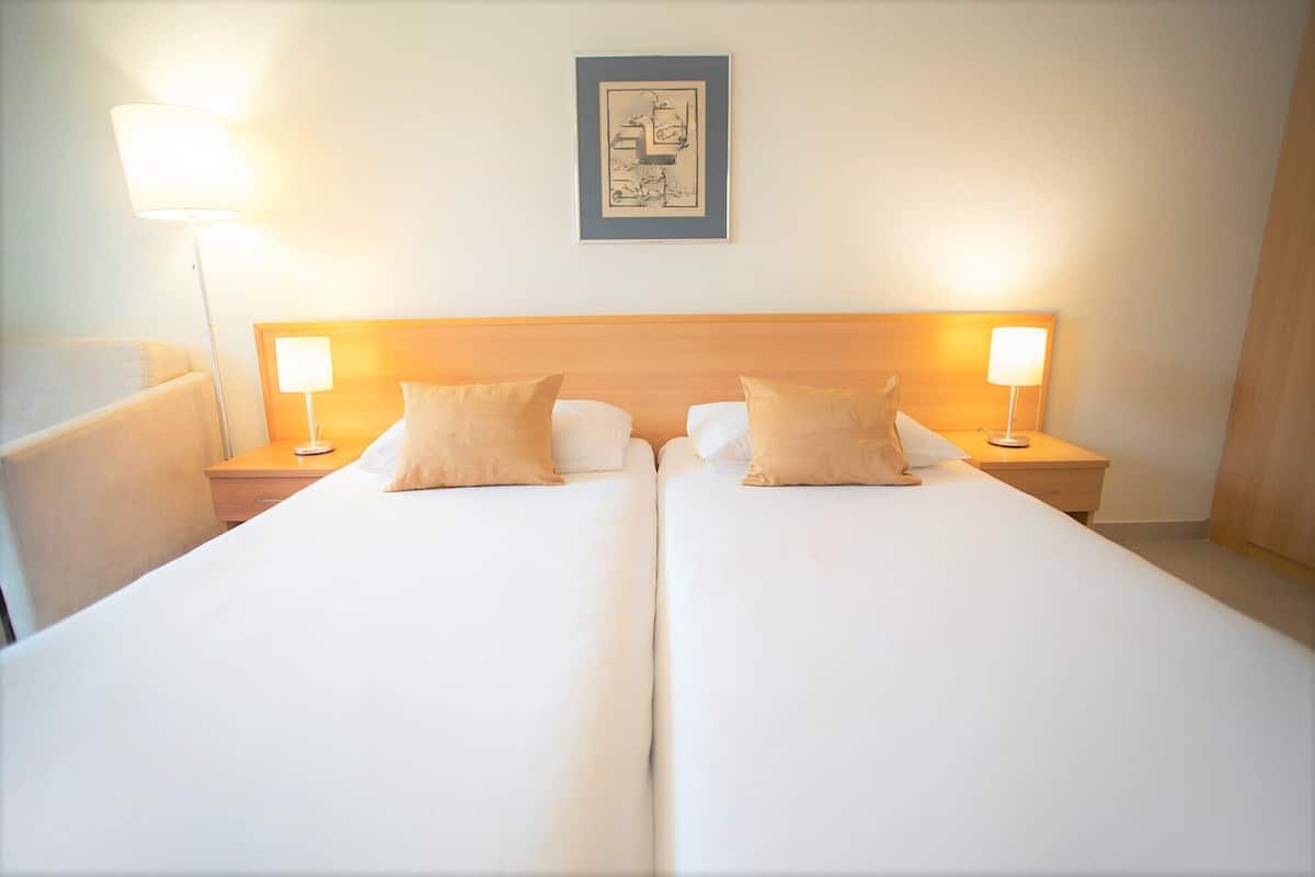 Una cama doble con dos mesitas de noche, cada una con una lámpara. Encima de la cama, un cuadro enmarcado cuelga de la pared.