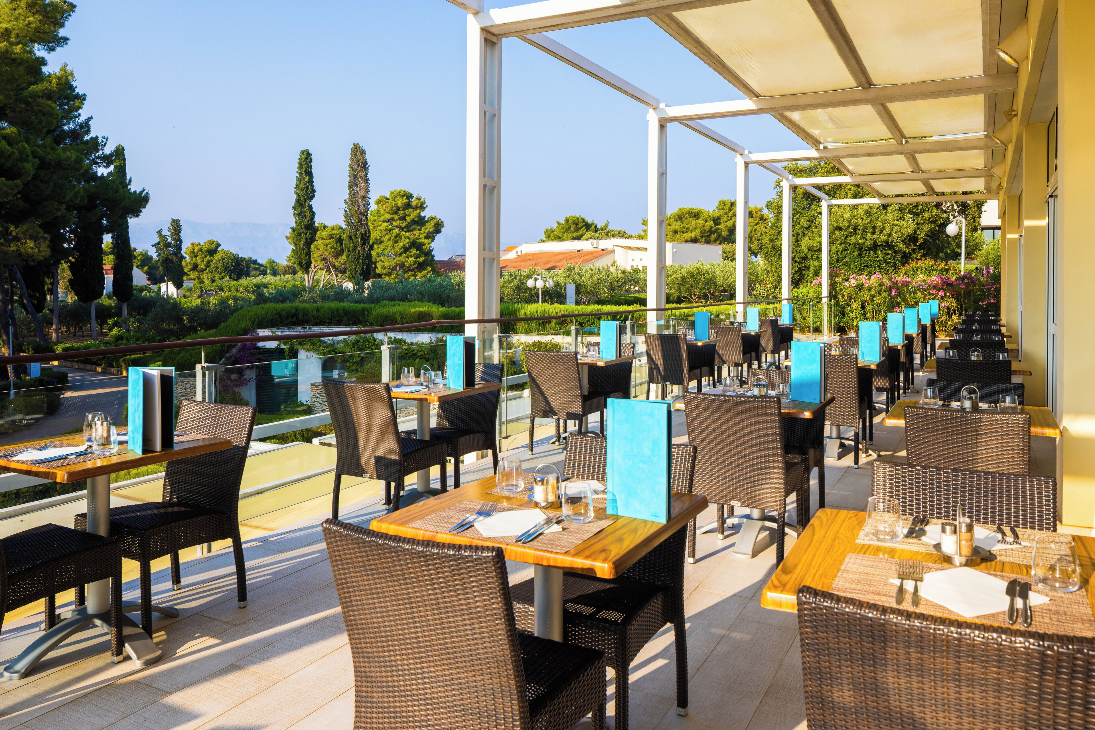 Un restaurante al aire libre con mobiliario de mimbre y vistas a la vegetación y montañas circundantes.