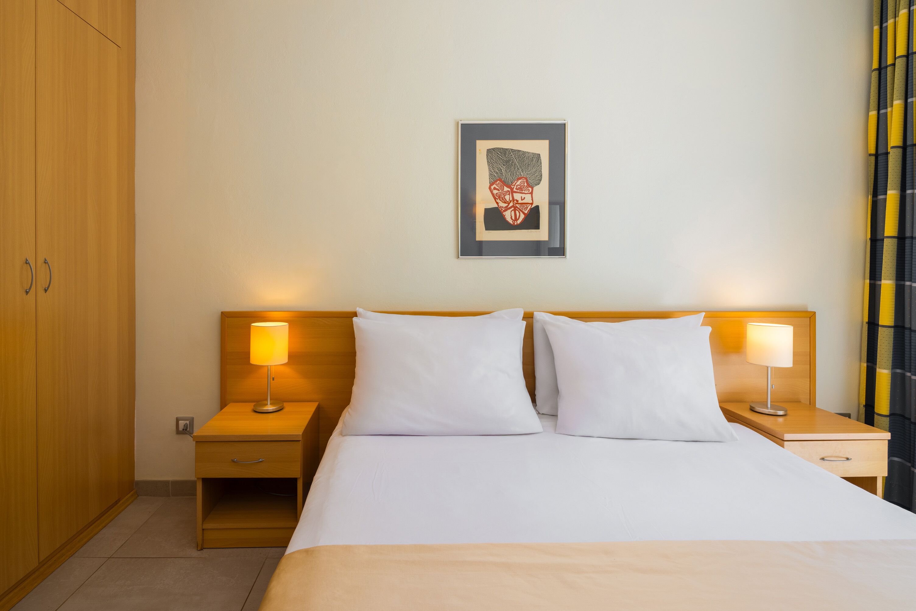 Une chambre d’hôtel comprenant un lit, deux tables de chevet avec des lampes, une armoire en bois et une œuvre d’art encadrée accrochée au mur.