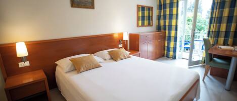 Une chambre d’hôtel avec un grand lit, une tête de lit en bois, deux tables de chevet avec des lampes, une armoire en bois et une vue sur l’extérieur grâce à une porte vitrée.