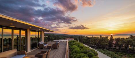 A rooftop terrace with outdoor seating and a view of the sunset over the sea.