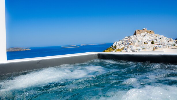 A coastal town with white buildings, a prominent hilltop structure, and a view of the sea.