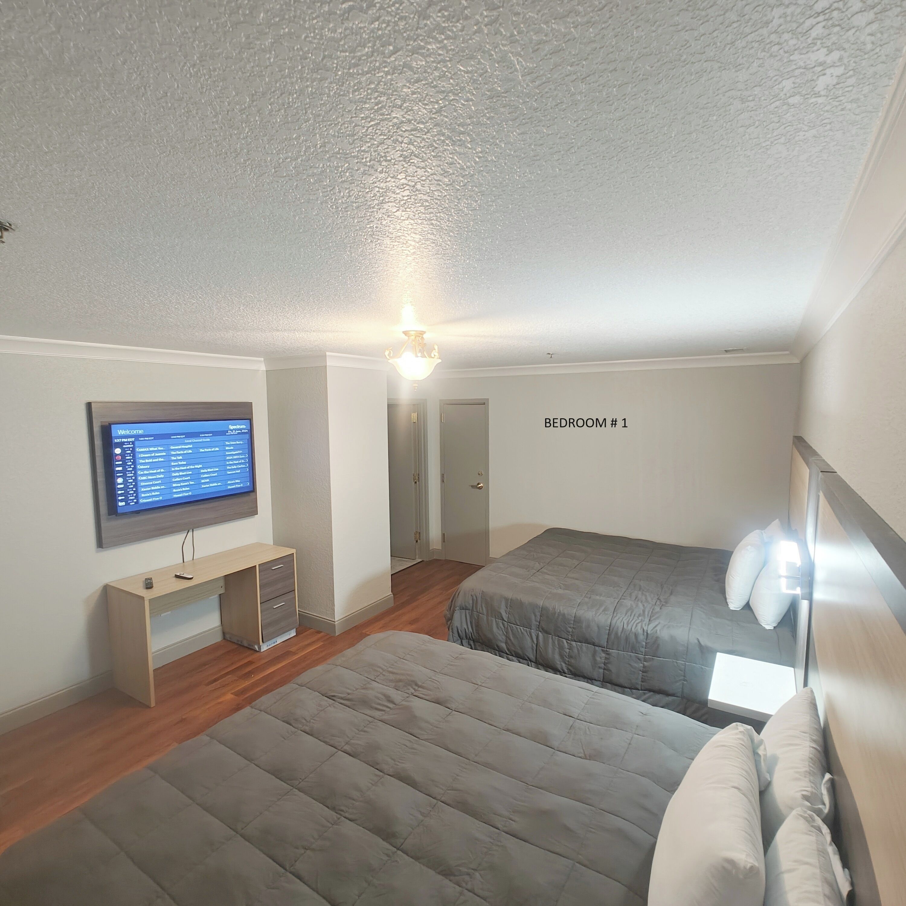 A bedroom with two beds, a desk, and a TV on the wall.