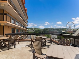 A balcony with outdoor seating, a view of a Ferris wheel, and a building in the background.