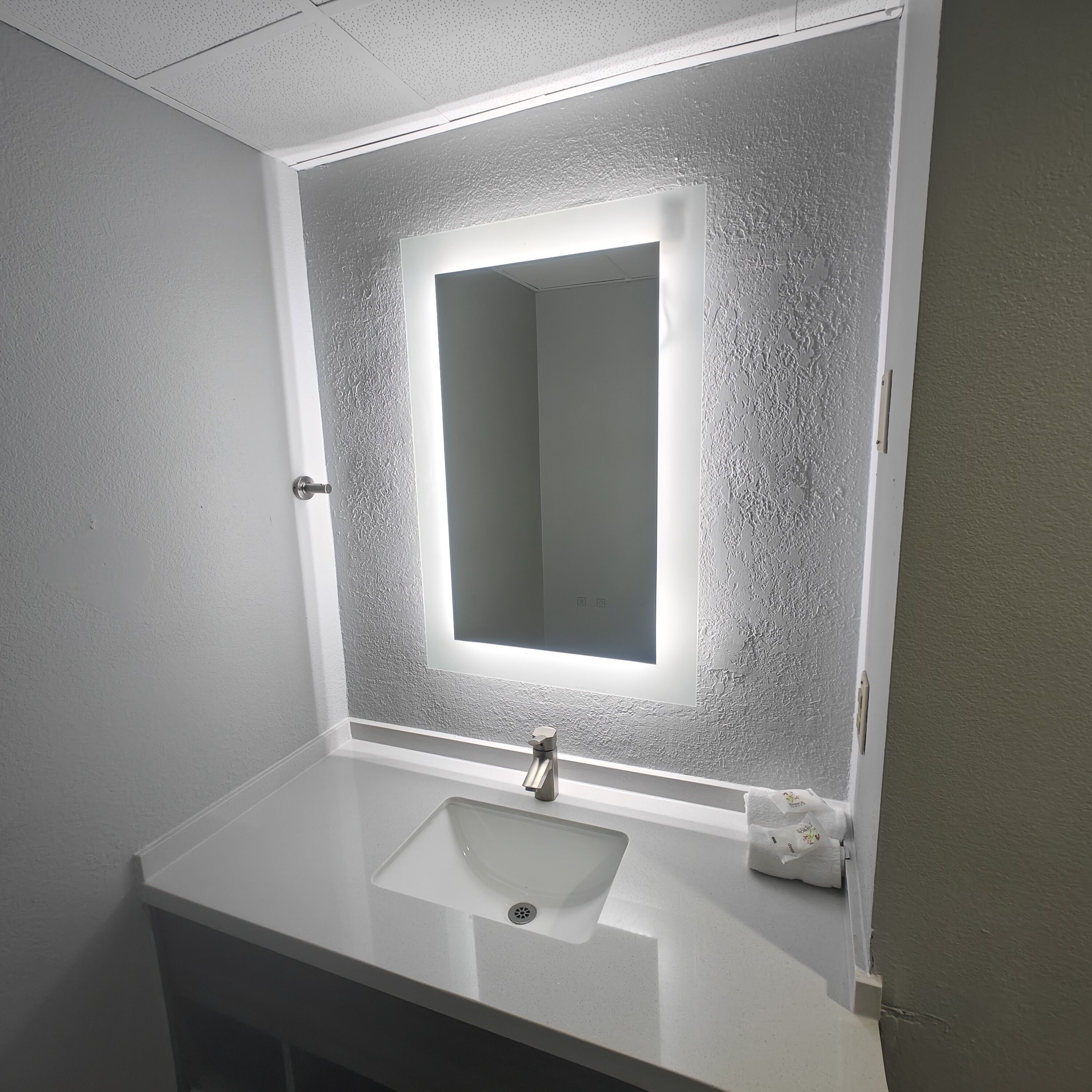 A bathroom with a white sink, a mirror with a light, and a towel dispenser.