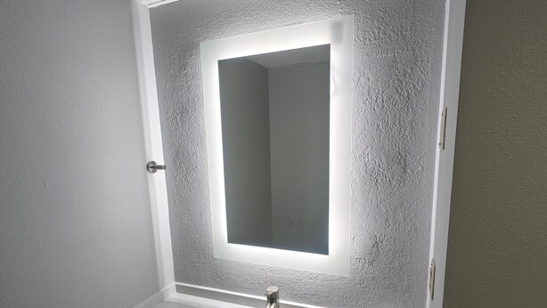 A bathroom with a white sink, a mirror with a light, and a towel dispenser.