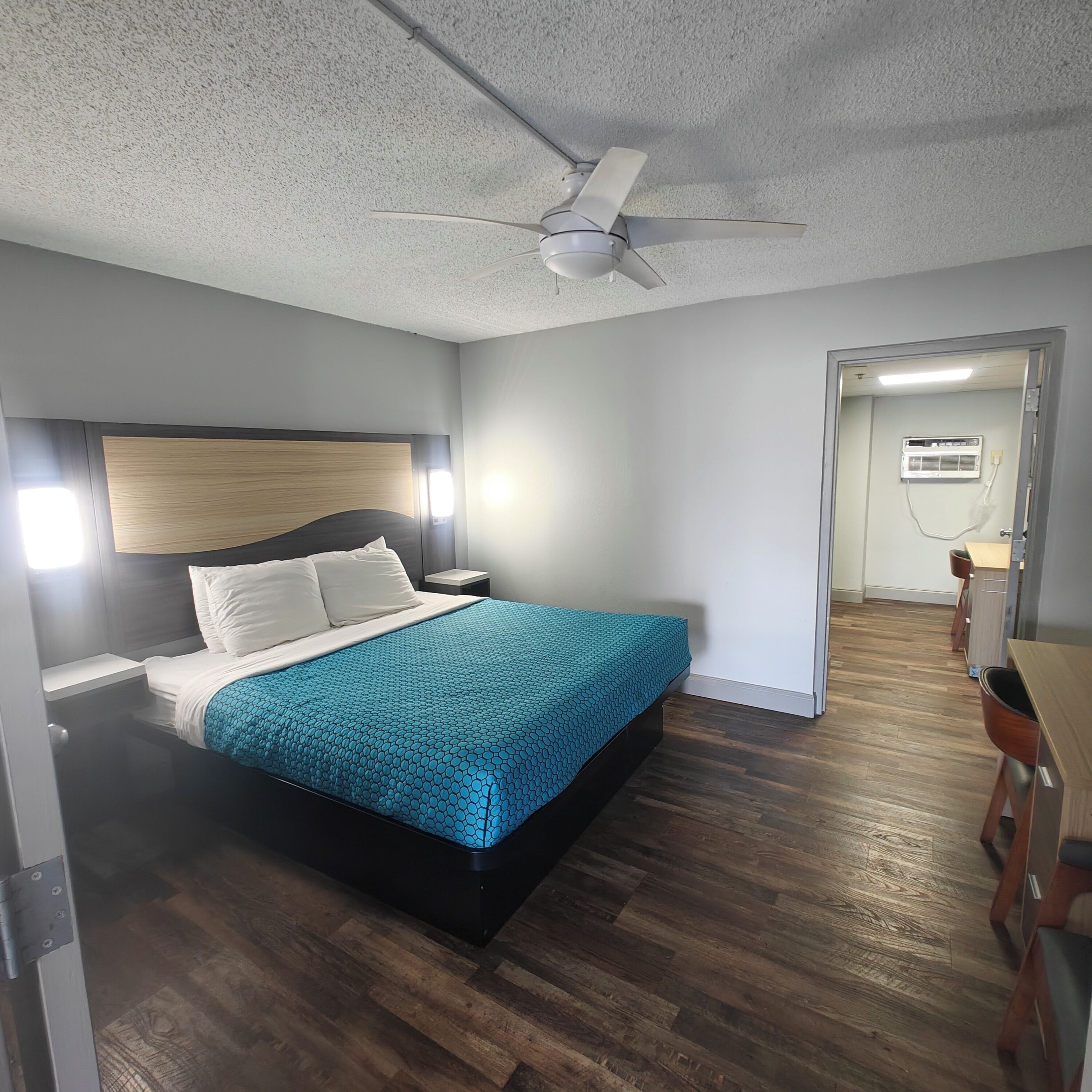 A bedroom with a bed, a ceiling fan, a nightstand, a desk, and a chair.
