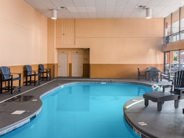 An indoor swimming pool with blue tiles, surrounded by chairs and a bench.