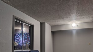 A modern living room with a dark blue sofa, a small coffee table, and a large window displaying a Ferris wheel. - Mountain Vista Inn & Suites (Pigeon Forge)