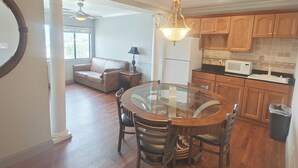 A spacious living room with a glass dining table, wooden chairs, a leather sofa, and a ceiling fan. - Mountain Vista Inn & Suites (Pigeon Forge)
