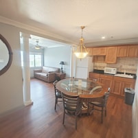 A spacious living room with a glass dining table, wooden chairs, a leather sofa, and a ceiling fan.
