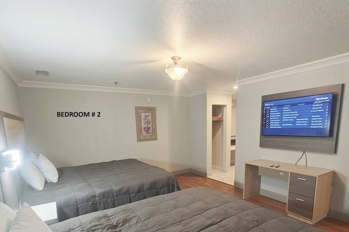 A bedroom with two beds, a TV, and a desk.