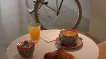 Een ontbijttafel met een croissant, een kop koffie, een glas sinaasappelsap en een klein bakje, met een fiets op de achtergrond.