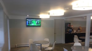 Une pièce avec un téléviseur fixé au mur diffusant un match de golf, plusieurs tables rondes avec des chaises et un coin cuisine.