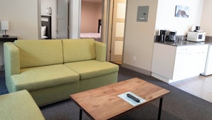 Un espace de vie compact comprenant un canapé vert, une table basse en bois et un coin cuisine équipé d’un four à micro-ondes et d’une machine à café.