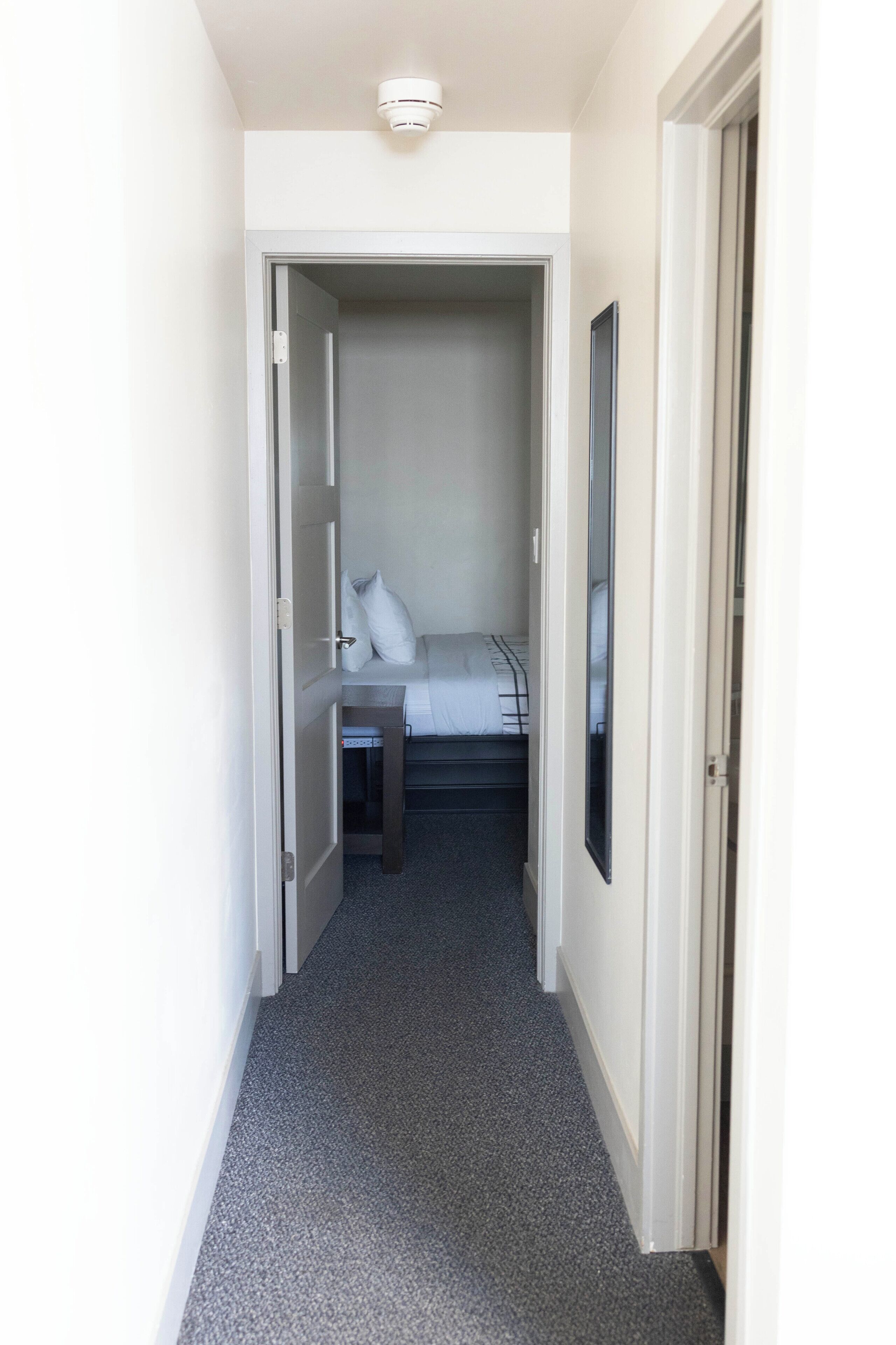 A narrow hallway leading to a bedroom with a bed, a bedside table, and a wardrobe.