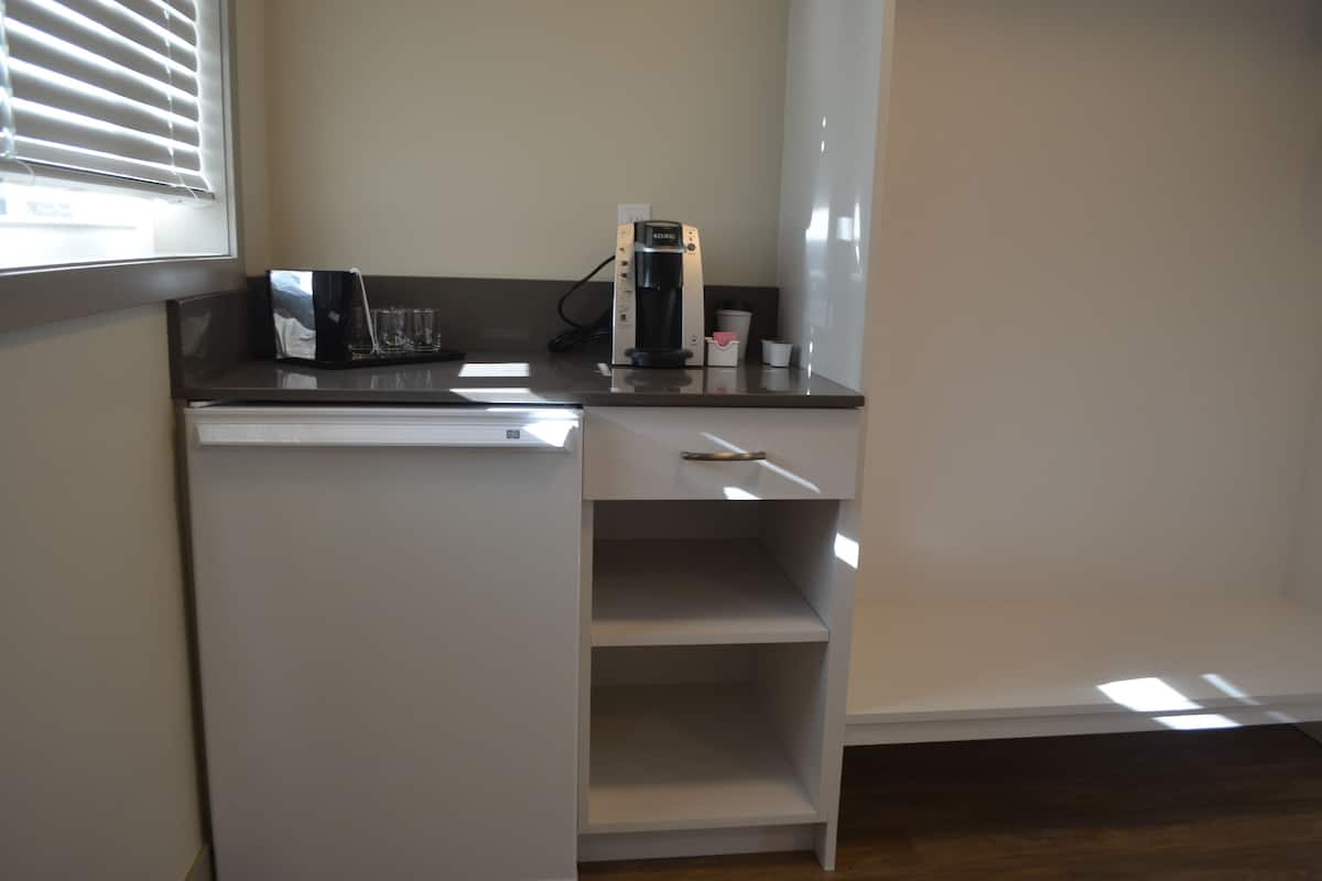 Una kitchenette compacta con una cafetera, una copa y una taza sobre la encimera.