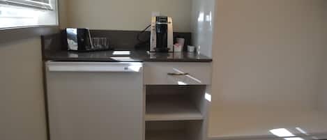 Et lille tekøkken med kaffemaskine, et glas og en kop på bordpladen.