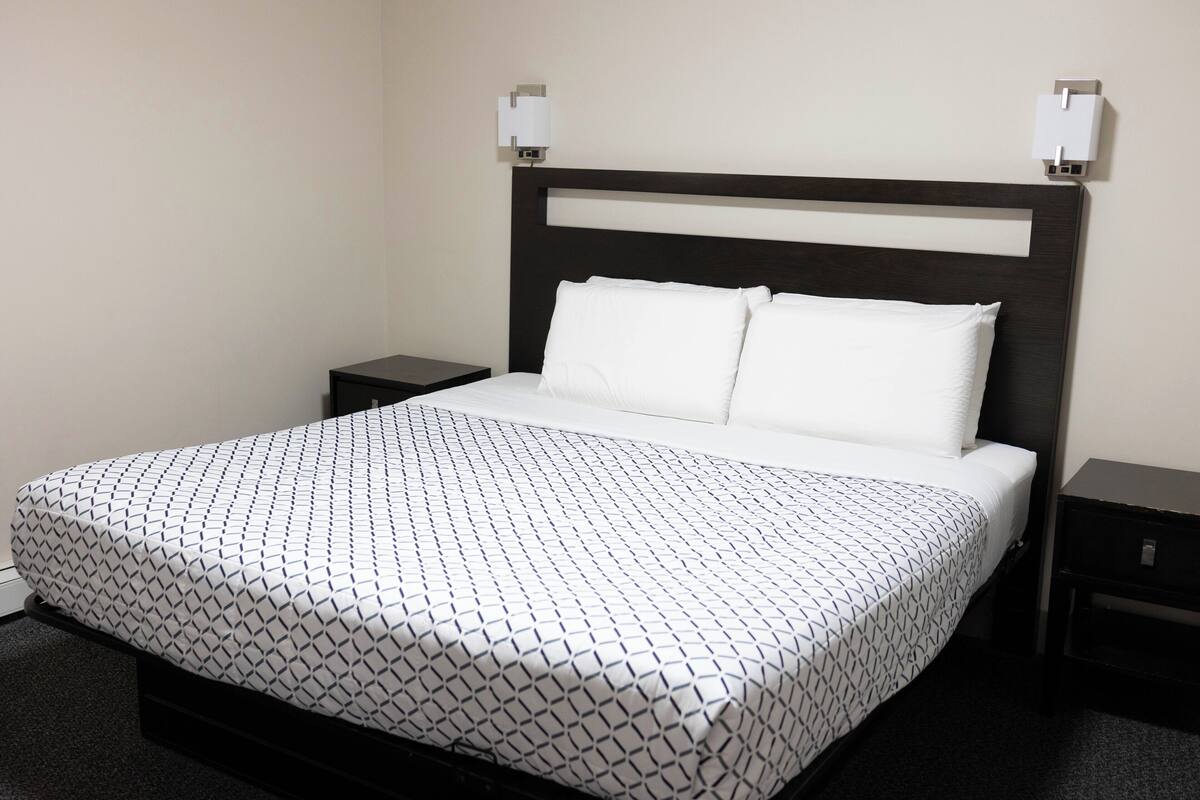 Una cama bien hecha con una colcha estampada y dos almohadas blancas, flanqueada por dos mesitas de noche con lámparas.