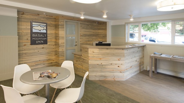 Un intérieur moderne avec un mur d’accent en bois, un comptoir d’accueil et un espace détente comprenant une table et des chaises.