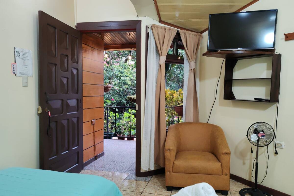 Una habitación con cama, una silla, un televisor y un ventilador.