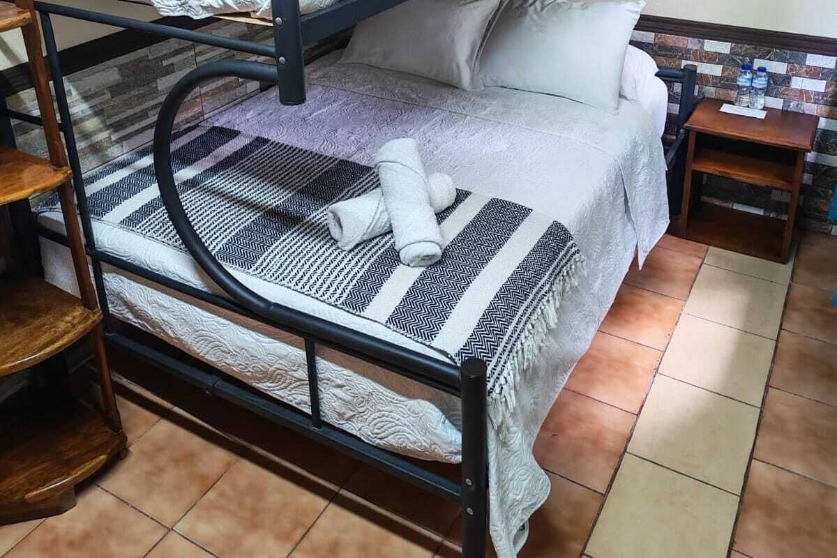 Dormitorio con literas, suelo de baldosas, una mesita de madera y un adorno en la pared.