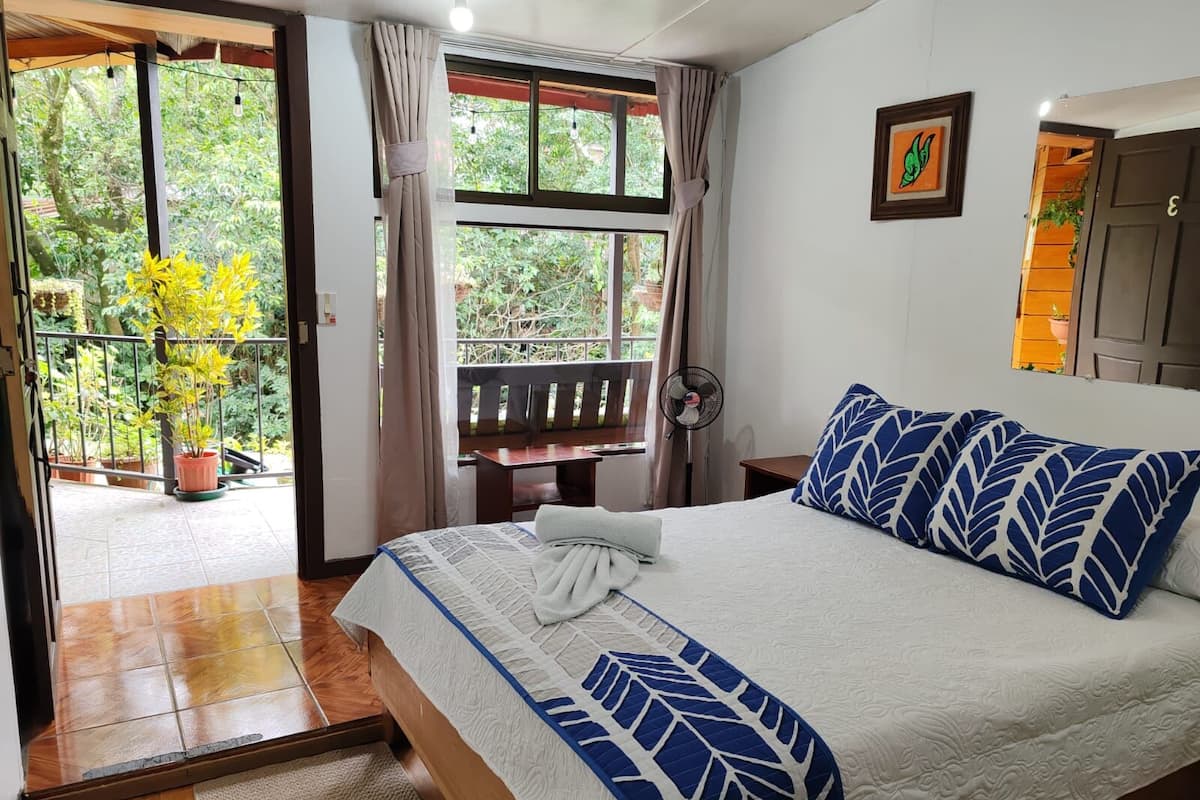 Un dormitorio con cama, escritorio y vistas a un balcón con plantas.