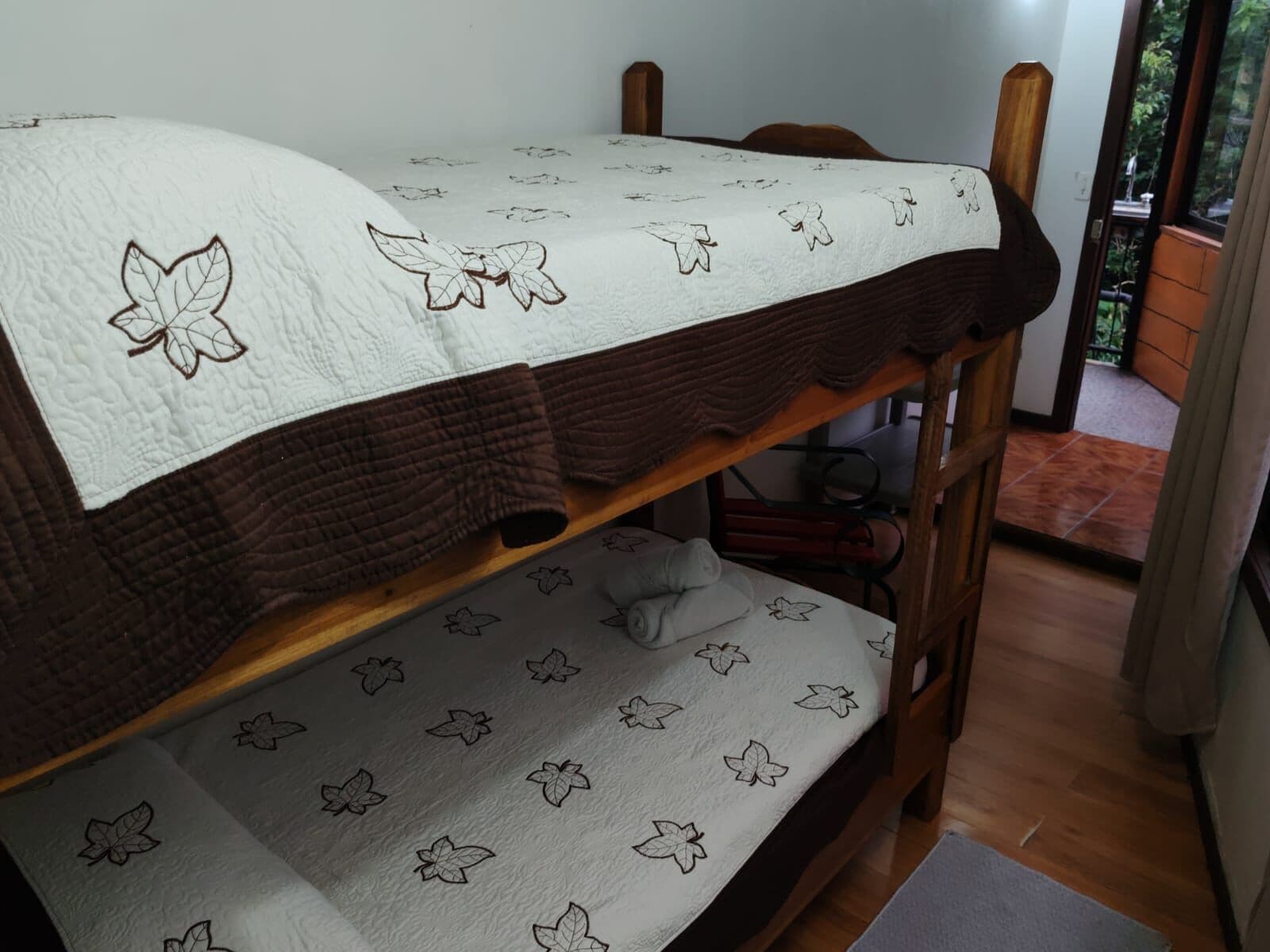 Una cama litera con un edredón blanco con motivos de hojas y un edredón marrón.