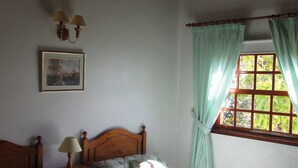 Camera da letto con due letti, soffitto in legno, una finestra con tende, una lampada a parete e un quadro incorniciato.