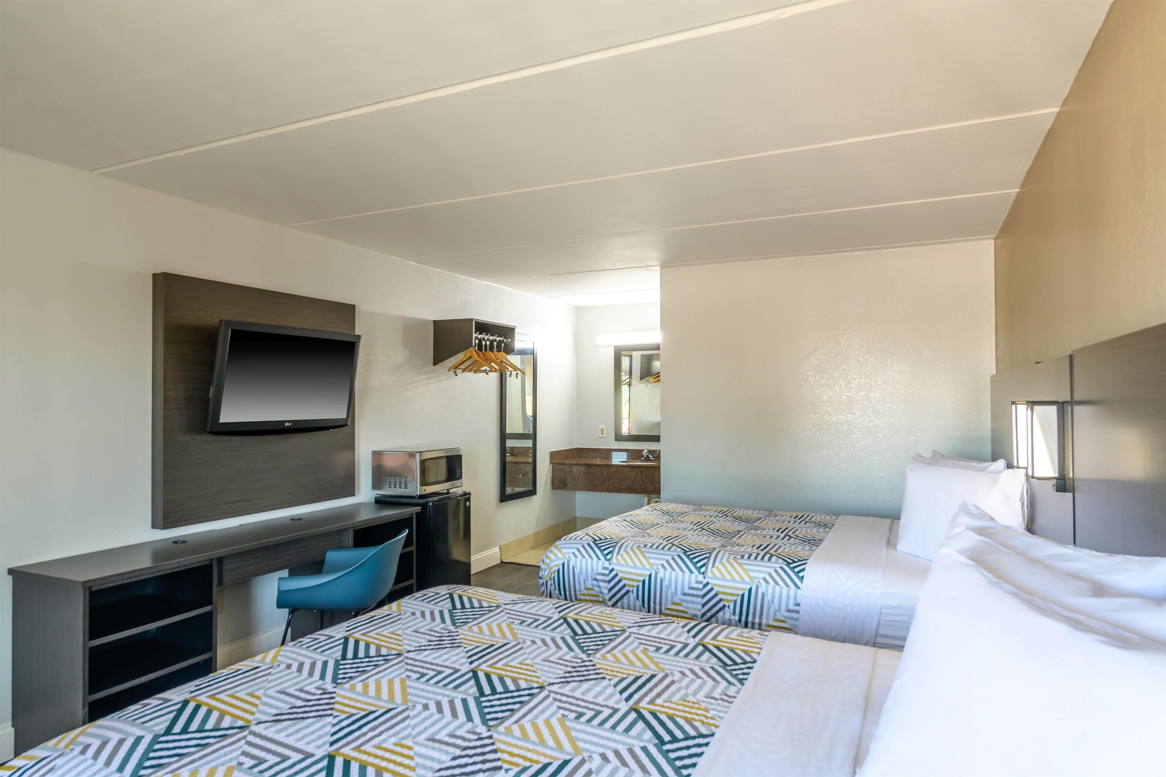 Ein Hotelzimmer mit zwei Betten, einem Schreibtisch, einem Fernseher und einem Badezimmer.