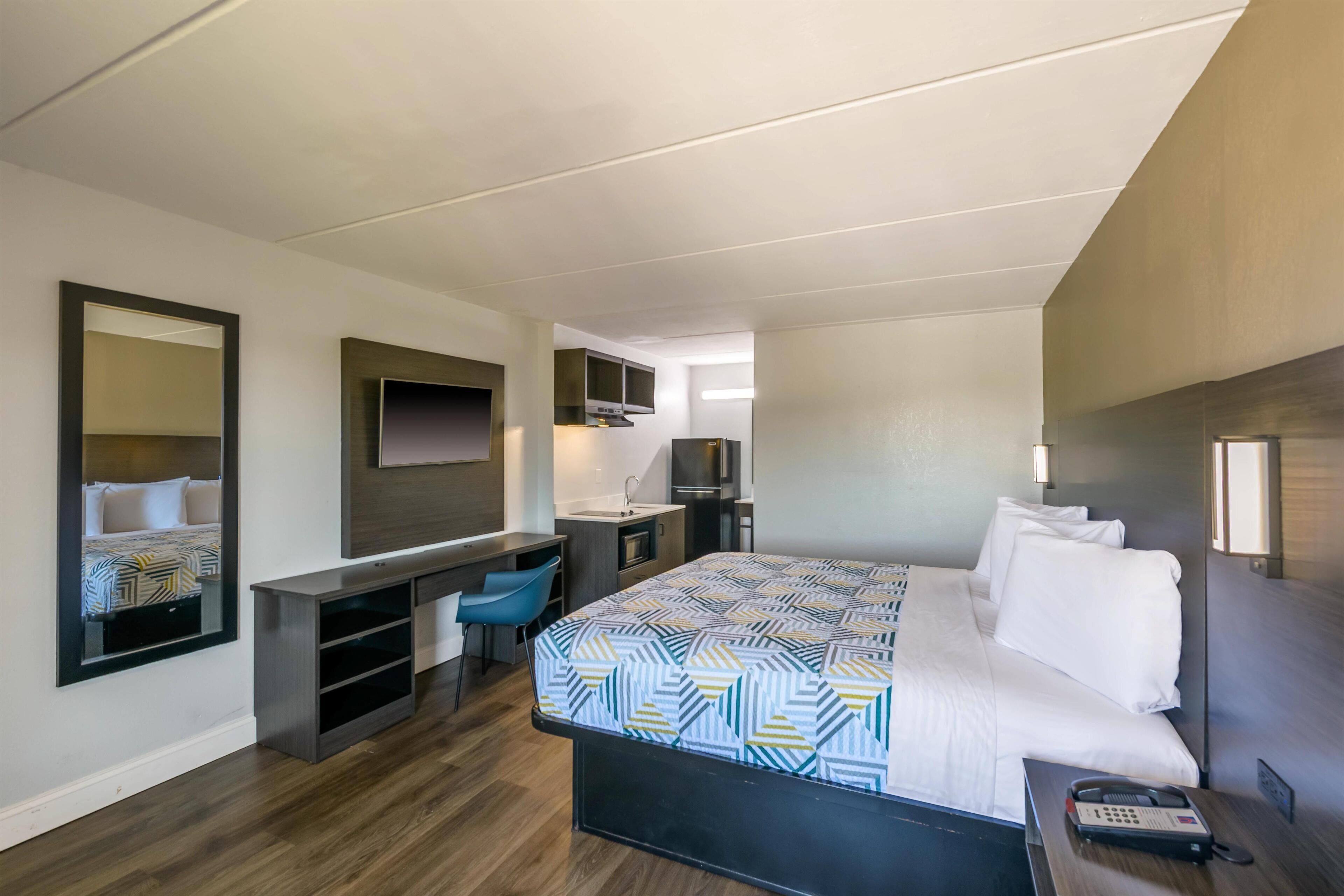 A hotel room with a bed, a desk, a chair, a TV, and a phone.
